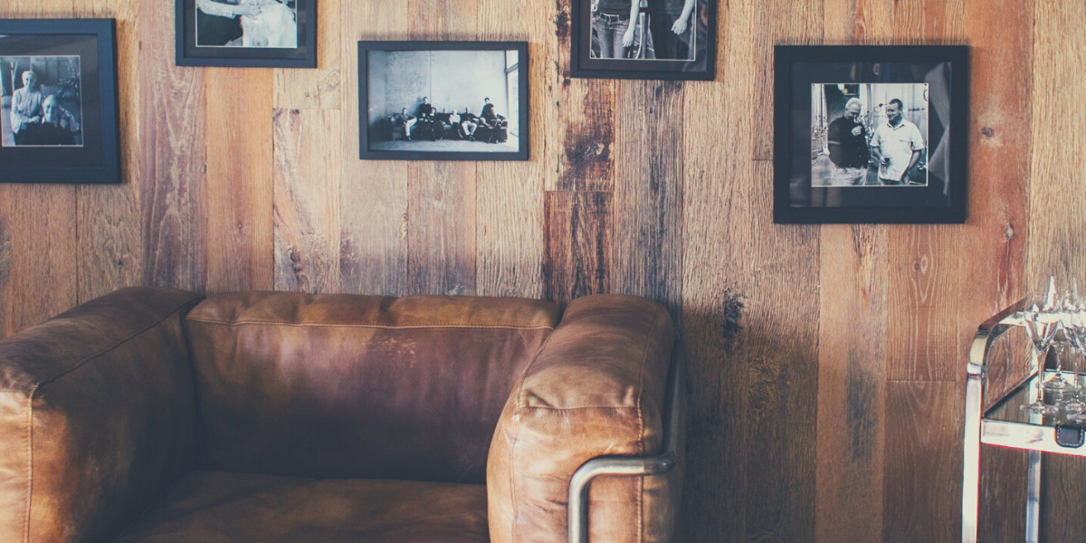 A brown leather one-seater couch sits against a wooden panelled wall dotted with black and white photos hanging in black frames.