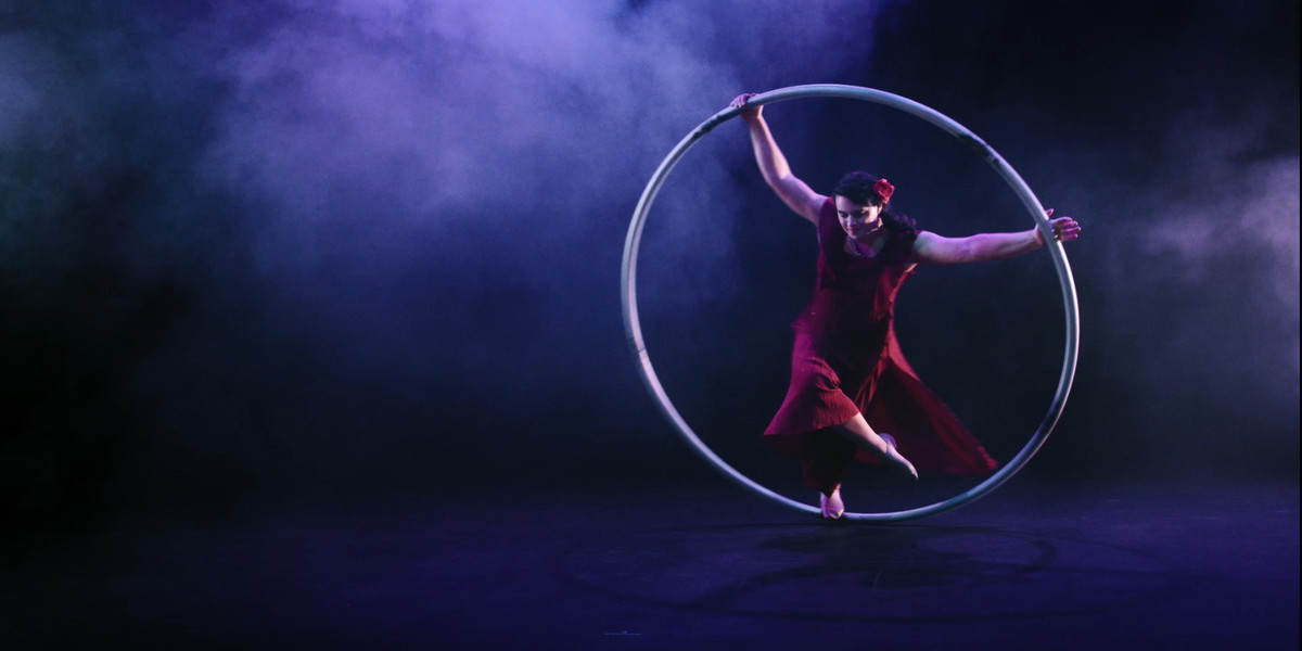 A women wearing a red dress spins in a giant hoop on a smoke filled stage.