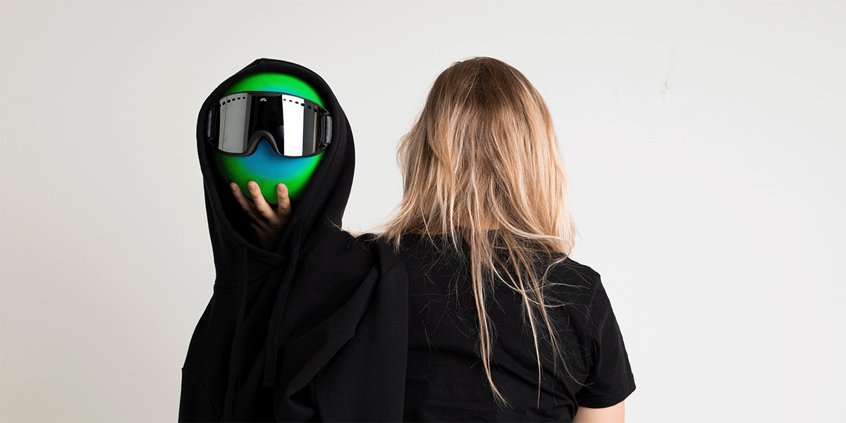 A woman facing backwards holding a ball with a ski mask on inside a hoodie