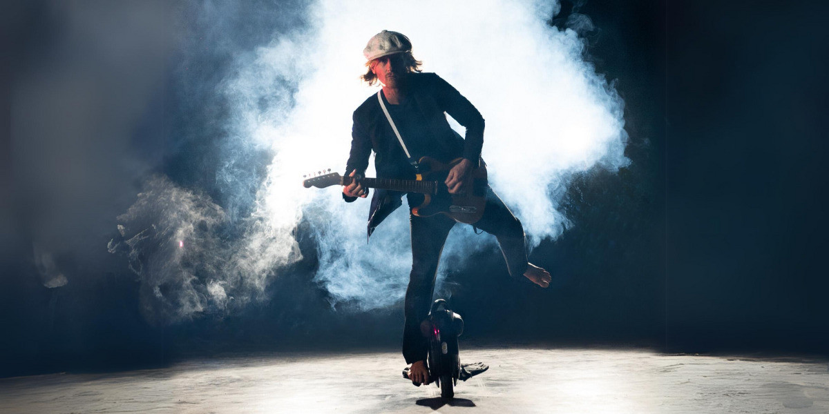 Guy balancing and holding a guitar with smoke behind him