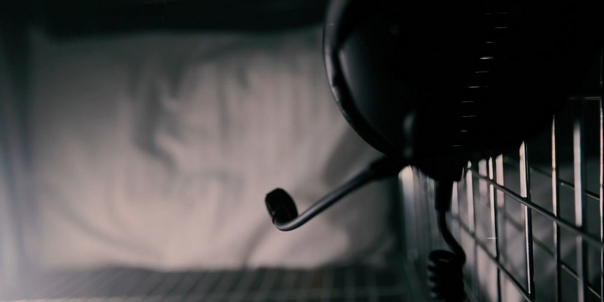 A close up photo of a pair of headphones on a metal cage with a white pillow in the background.