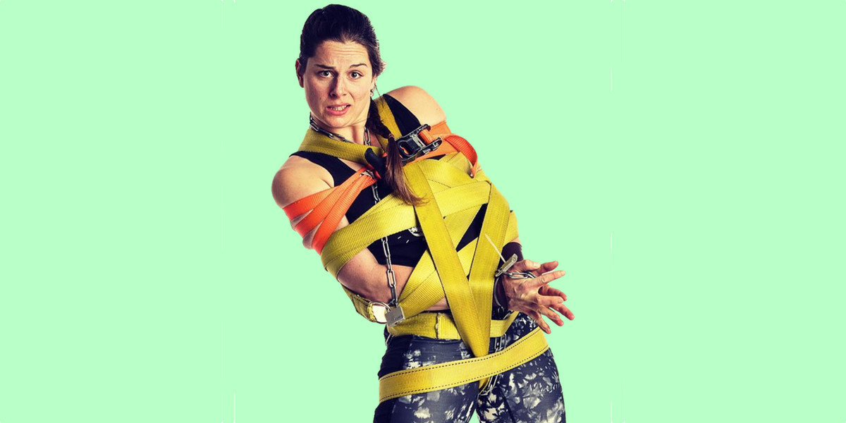 Woman with brown hair, tied up in brightly coloured yellow and orange straps and chains on a green background.