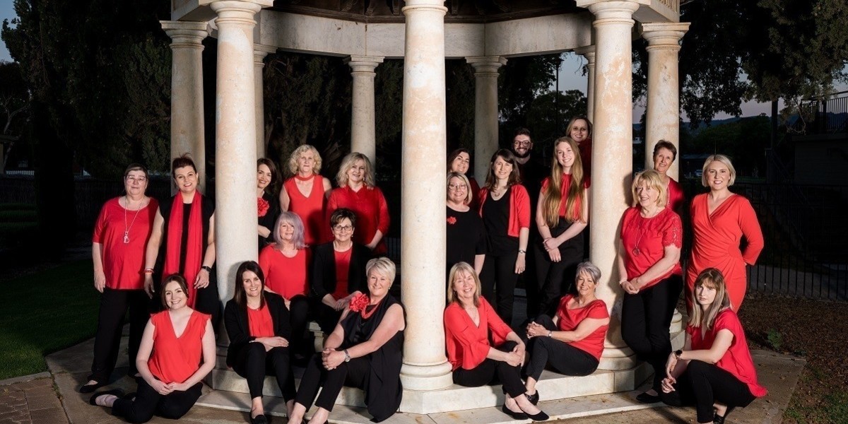 Members of High Spirits Harmony, dressed in red and black, stand and sit around a band rotunda.