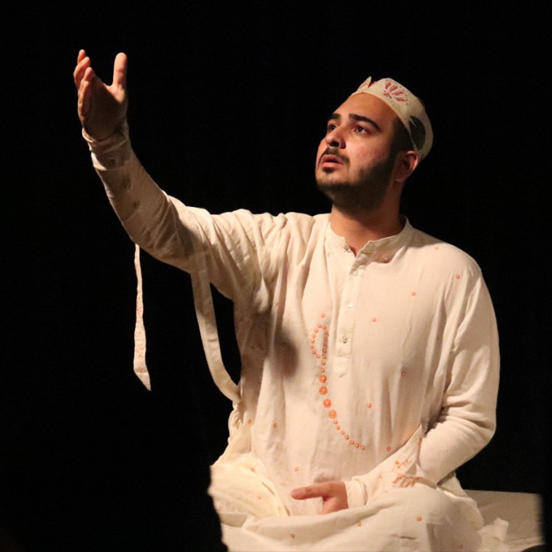 Indian man seated dressed in a white gown with one hand raised