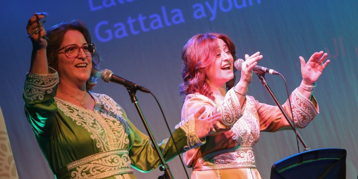 Two female singers, singing and dancing, dressed in colorful traditional Arabic dress.