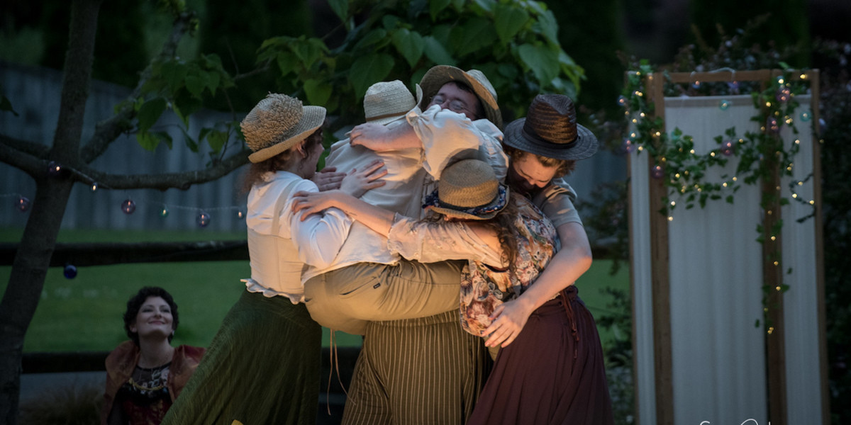 The cast of The Barden Party as The Mechanicals in A Midsummer Night's Dream, crowded in a delightful group hug at dusk in a beautiful garden.