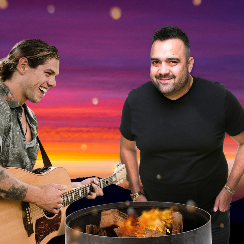 Two smiling men stand around a fire in a barrel. The man on the left is in a patterned shirt with the top buttons undone, he is playing an acoustic guitar. The man on the right has his hands in his pocket and wears a black t-shirt. The background is sunset colours starting from yellow blending through orange up to purple at the top.