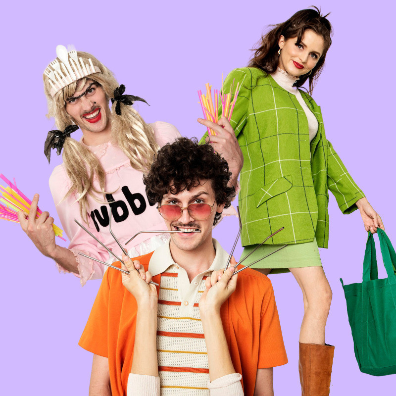 Three people.
On the left is a man wearing a pink dressing labelled rubbish and a messy wig with a crown made out of plastic cutlery on top.
In the middle is a ma wearing 70s clothing a bring orange jacket.
On the right is a woman wearing a green suit holding a reusable shopping bag.