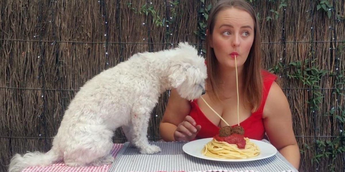 Emily Grace - Rooted - Emily Grace sharing a plate of spaghetti and meatballs with her dog. She and her dog have ends of the same strand of spaghetti in their mouths