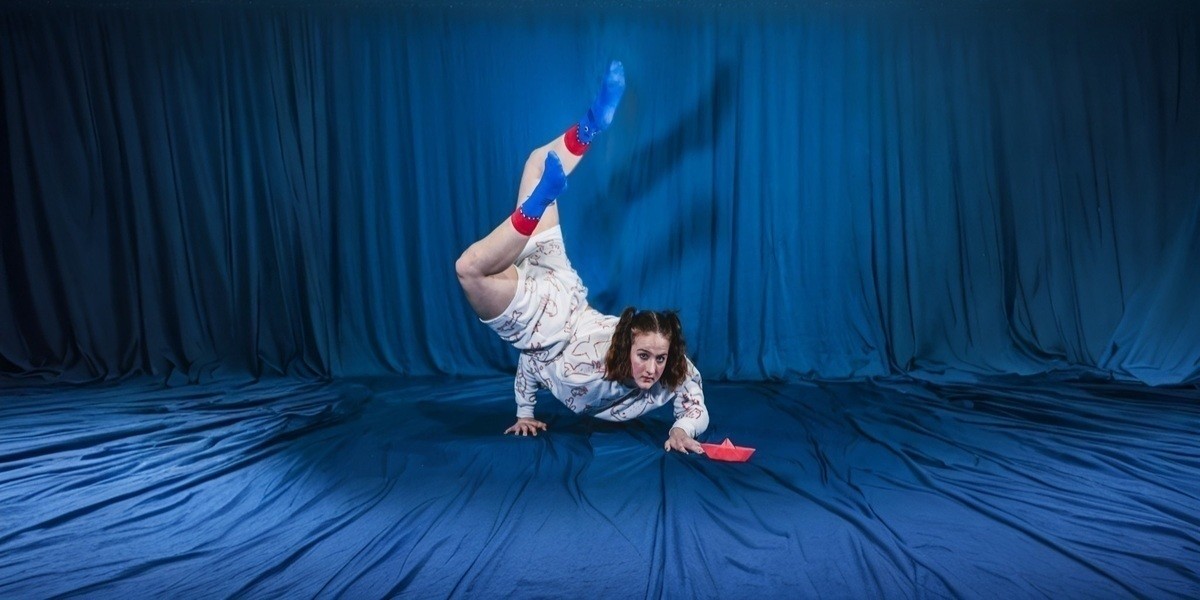 A Paper Trail - a performer does a handstand on a blue curtain
