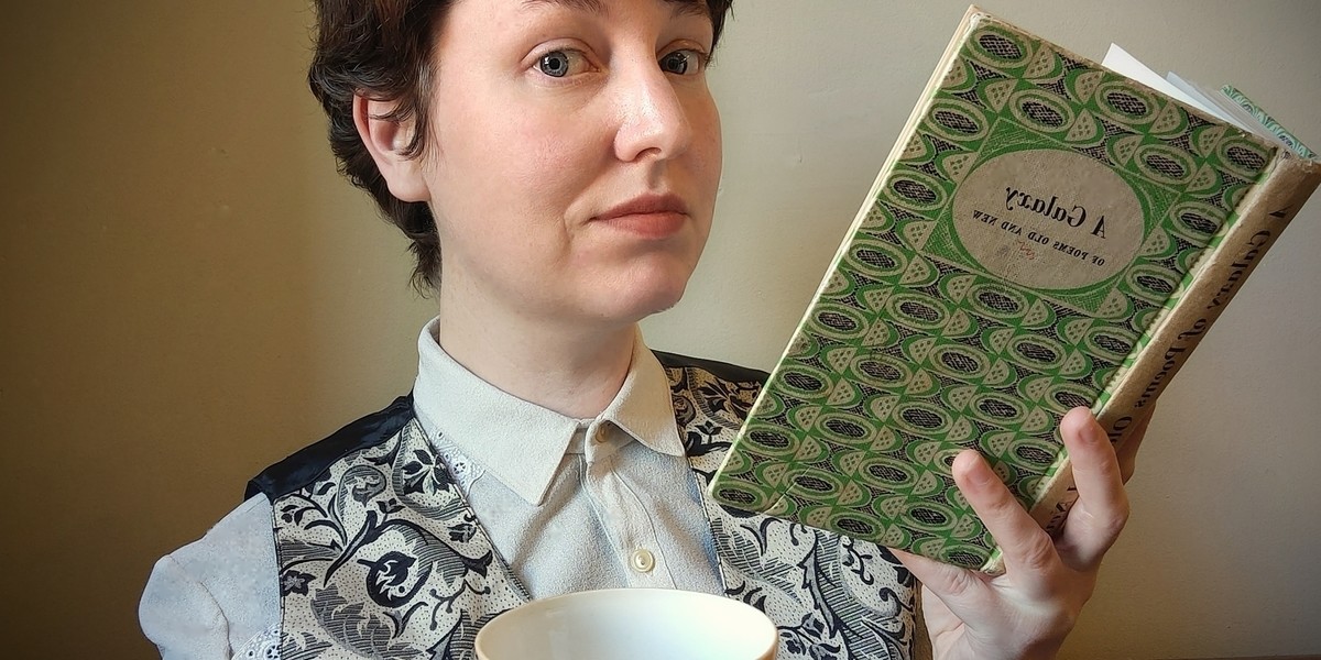 Tales in a Teacup - A dapperly dressed person is holding an open book in one hand. In the other hand they are holding out a teacup and saucer invitingly.