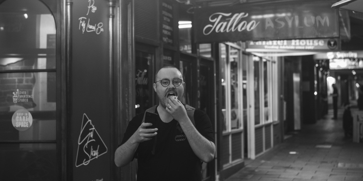 Comedian James Donald Forbes McCann on a street at night time, eating takeaway food.