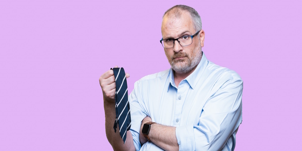 Rob Farley, a white man with a beard and glasses, has a raised eyebrow as he holds a school tie. He is in a light blue collared shirt.