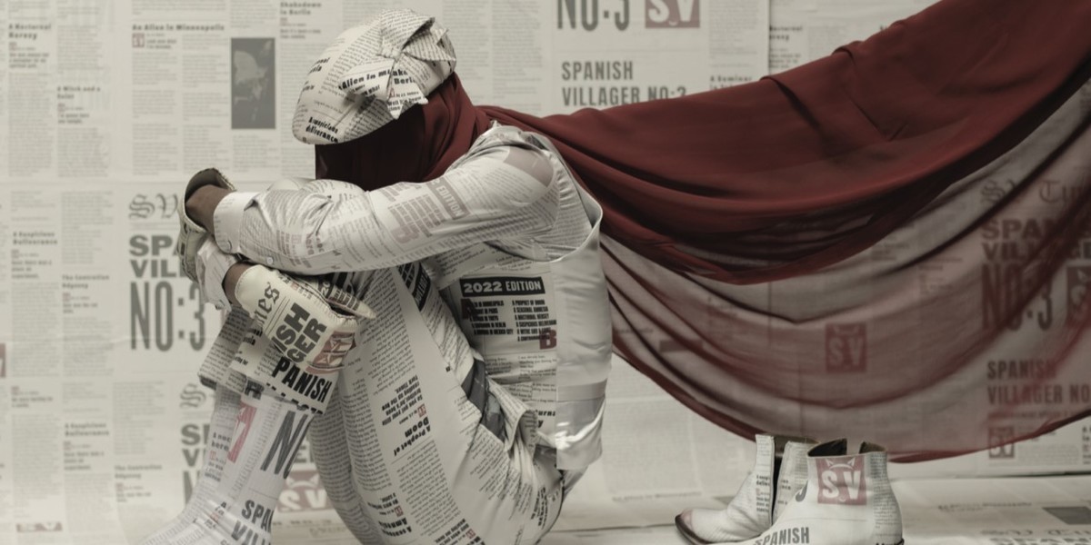 Ondara - Ondara dressed in a suit of newsprint and red scarf hiding his face.