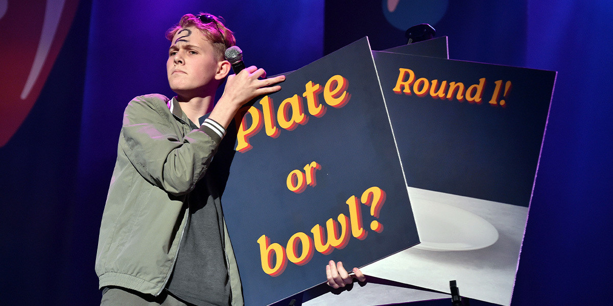 Young boy on stage, holding two signs, one that says round 1, the other says plate or bowl
