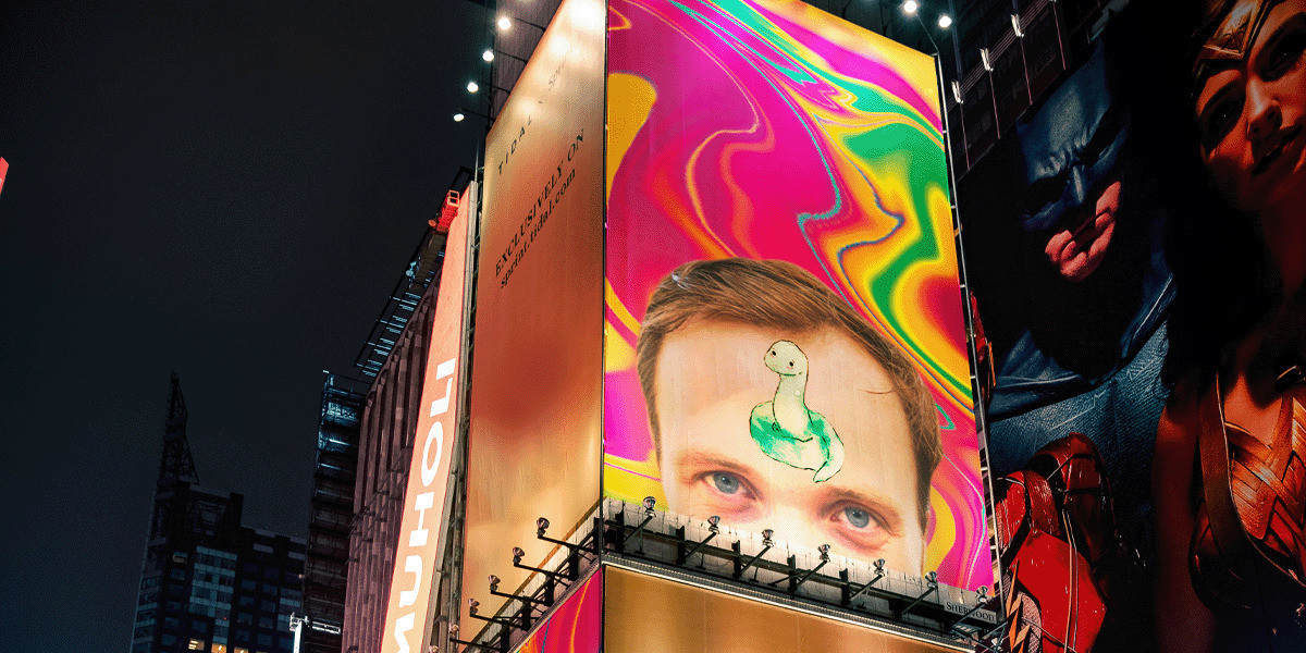 Snake Boy Takes Manhattan - A giant billboard in Times Square shows the image of "Snake Boy". You can see the top of performer Alexander Richmond's forehead and in the centre of his forehead is a small green cartoon snake.