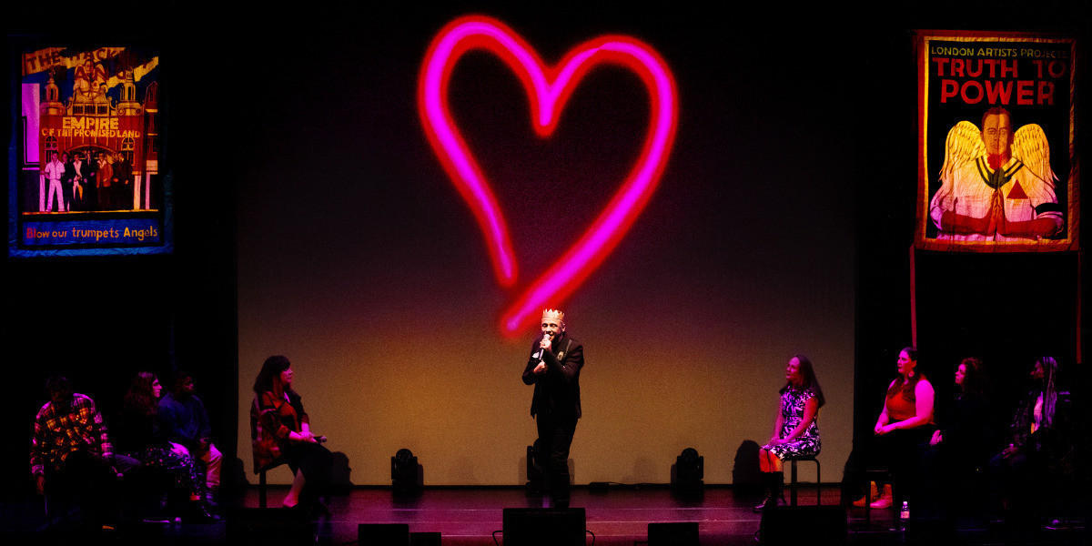 Jeremy Goldstein in a gold leather crown with participants in front of a large pink neon heart