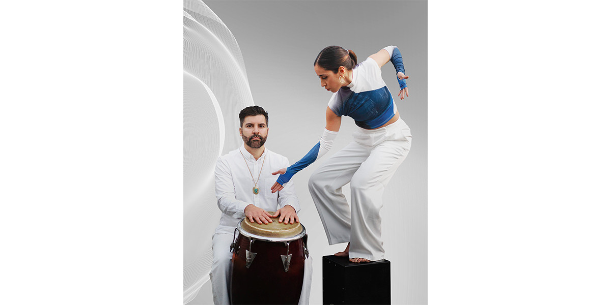 Individual dressed in white plays a drum, whilst another is caught mid dance.