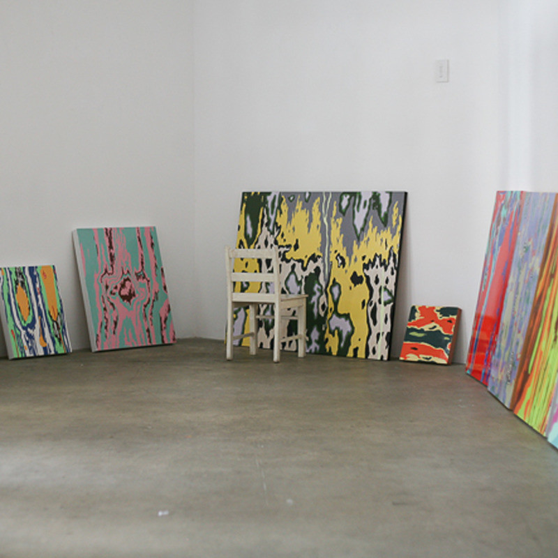 Conversations in Colour - In a studio space a number of brightly coloured abstract paintings sit on the floor, leading against the white wall. A white chair faces the largest canvas which is black white and yellow