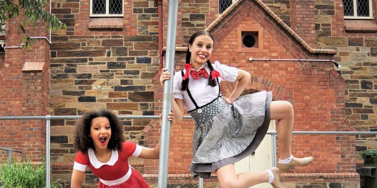 Annie in a bright red dress stands on the street with Matilda in a school uniform.