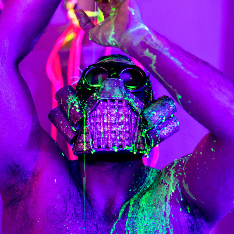 Liminal Treats - A man wearing a gas mask is bathed in purple light and is in a purple space. There is glowing green liquid dropping onto him and running down his body.
