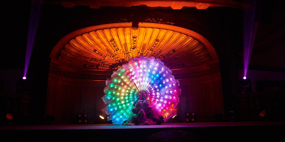 Jazida in a backbends holding LED feather fans lit up with rainbow colours