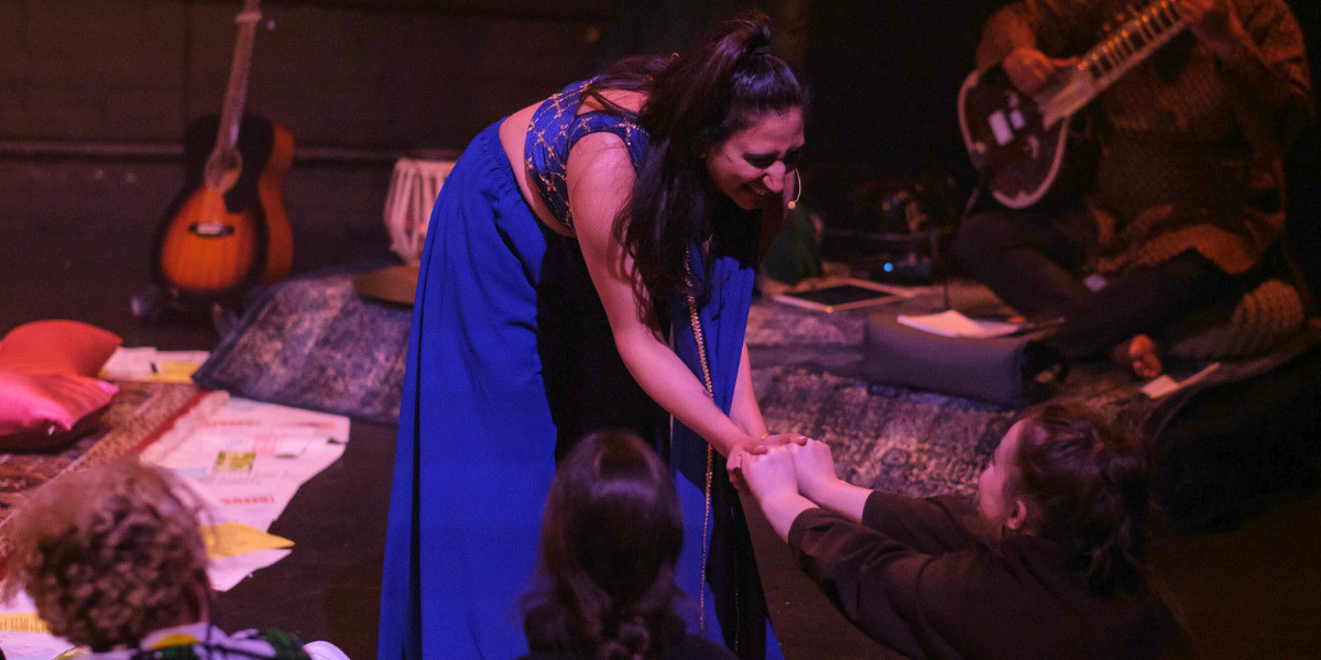 Performer, Almitra, leans forward to hold the hands of a woman in the front row of her audience.