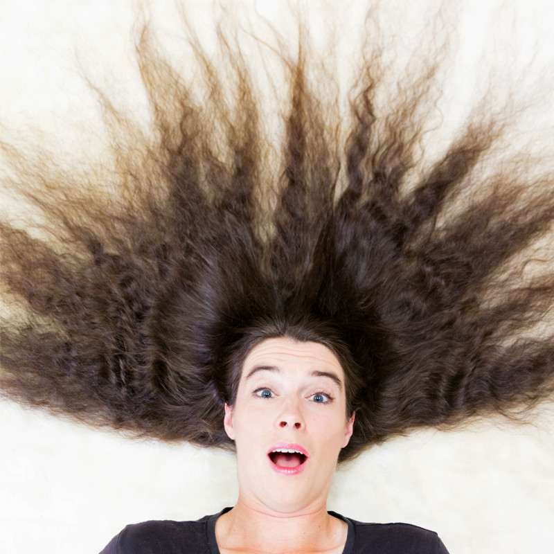 A caucasian woman, Luth, faces the camera with a shocked expression on her face. Her long brown hair spreads out in an explosion around her head, stretching to the edges of the image