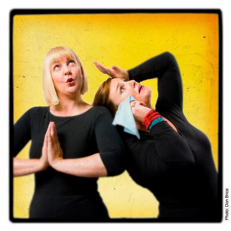 A photo of two women wearing black long sleeved t-shirts. The woman on the left has short blonde hair. Her hands are placed in a prayer position in front of her chest and she is pouting her lips. The woman on the right has a look of despair on her face and is holding a light blue hanky to her face.