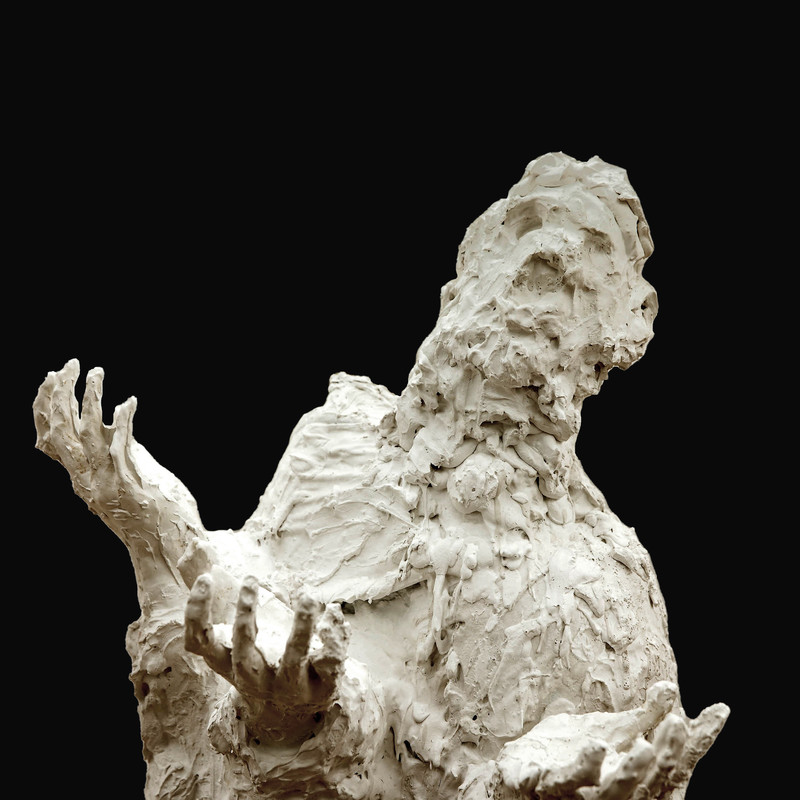 The Leftovers - A plaster scuplture stands amongst a black back drop. The statue has 3 hands and arms and an un-identifiable face.