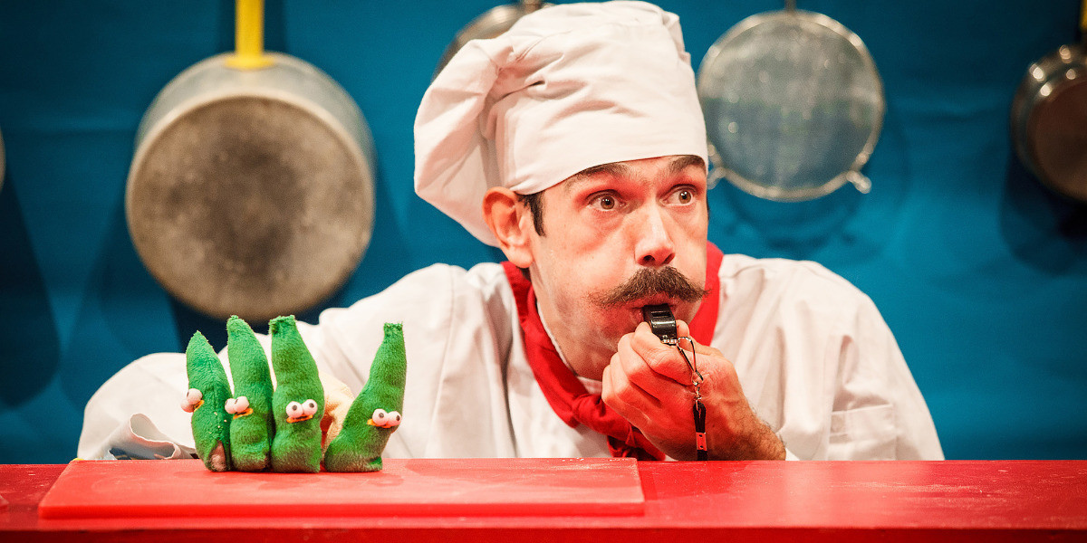A man in a chefs hat is blowing a whistle. On his fingers are four green finger puppets in the shape of beans.