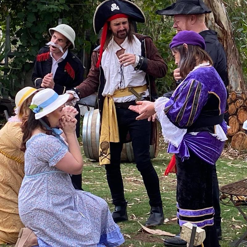 Cast of pirates kneels before the Pirates King who is recognisable by his pirate hat.