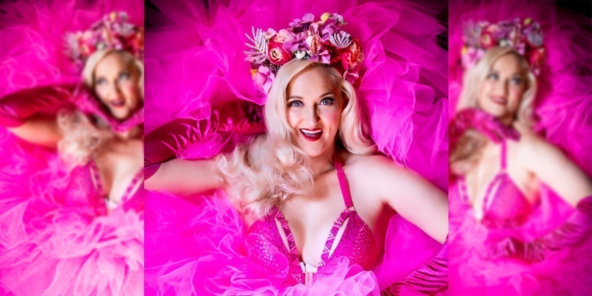 Barbie Burlesque - Blonde woman in pink skirt and headpiece smiling at the camera. She is dressed to resemble Barbie.