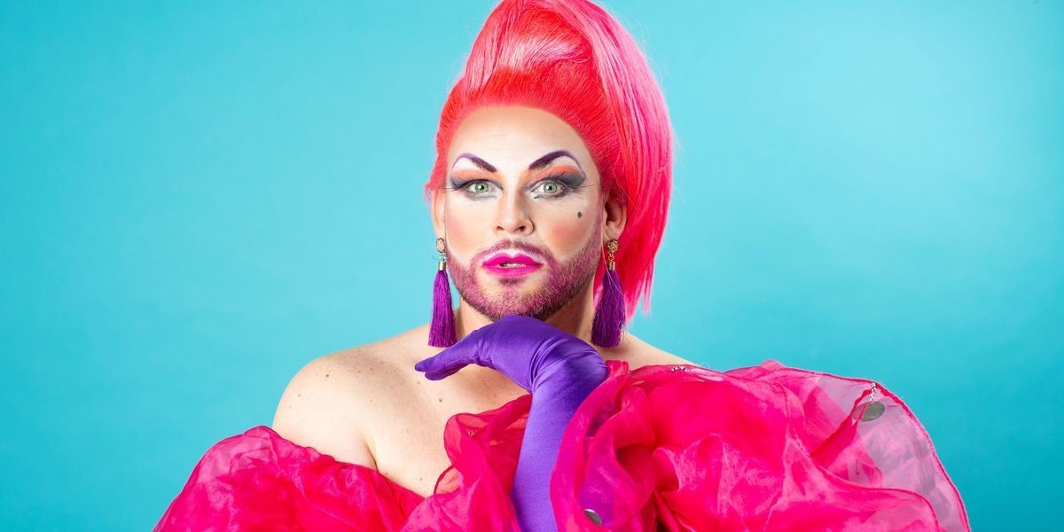 LEATHER LUNGS: SHUT UP AND SING! - A drag queen with pink hair and wearing a pink ruffled gown, shoots us a sultry look