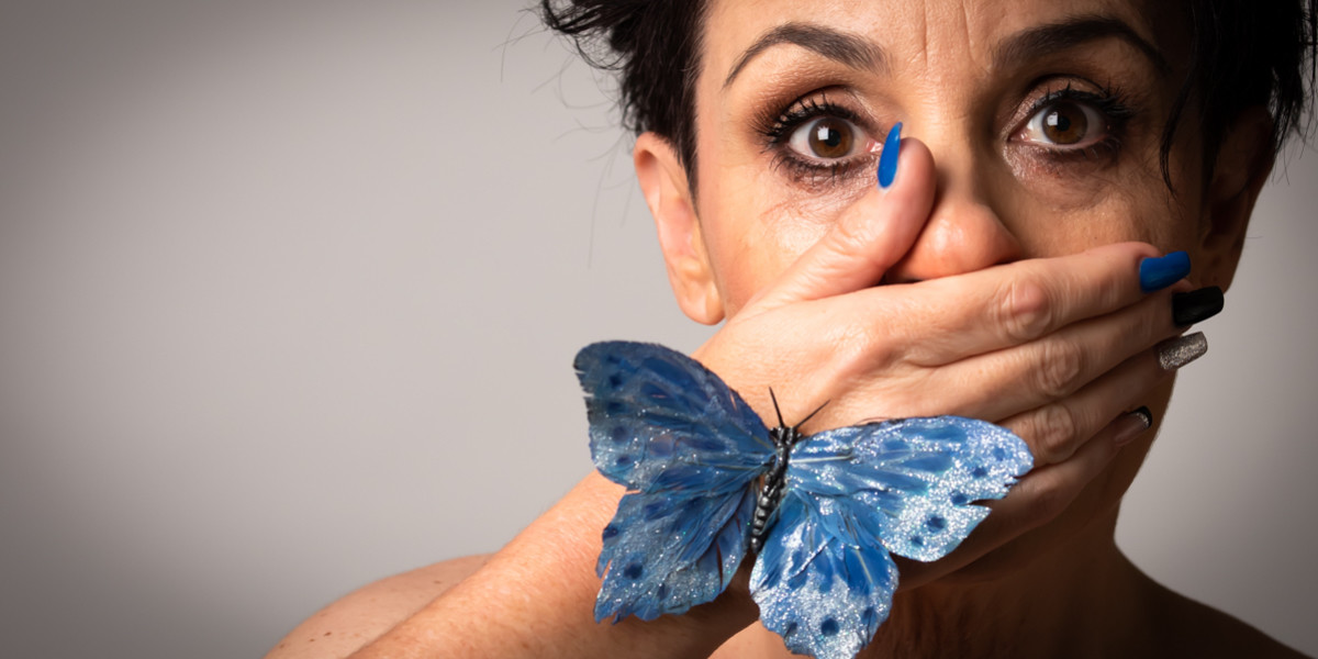 woman staring wide-eyed hand over mouth with a blue butterfly on her hand