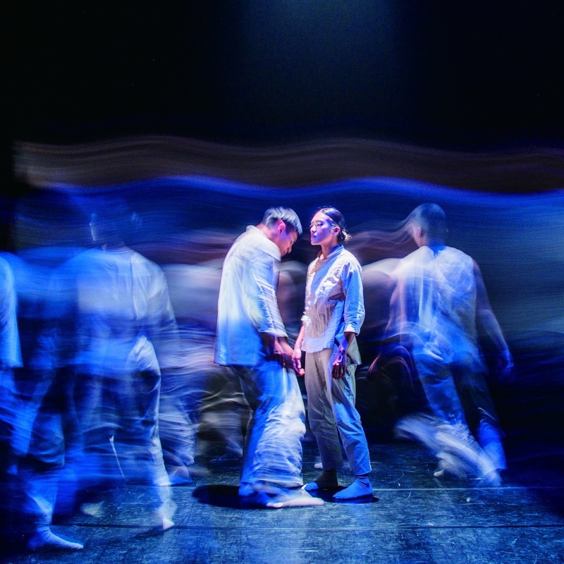 two dancers dace each other with blurred imagery of other dancers in the foreground and background
