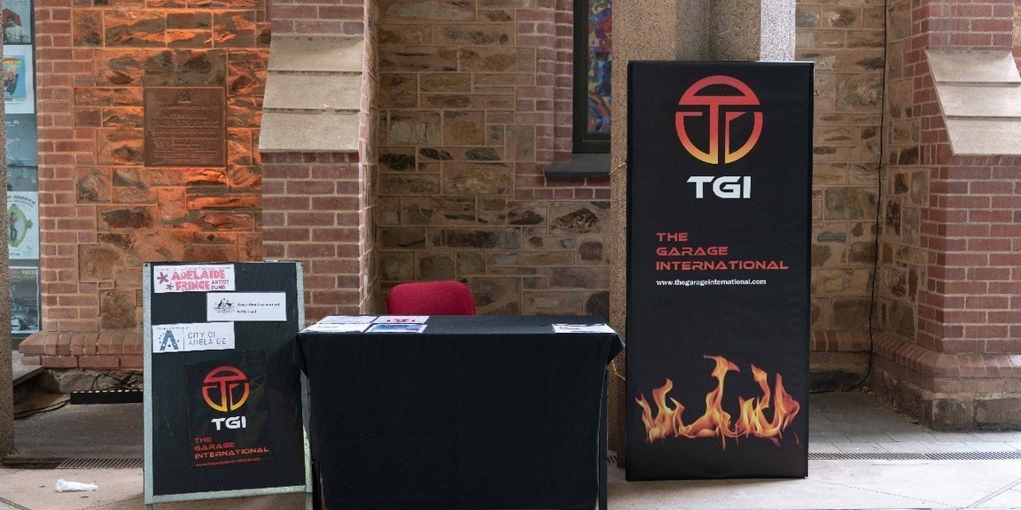 box office of TGI @ Adelaide TOwn Hall.  Black table with banner and A Frame.