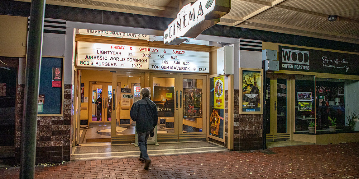 Man enters the cinema via 4 glass doors with a marquee displaying film names above the doors.